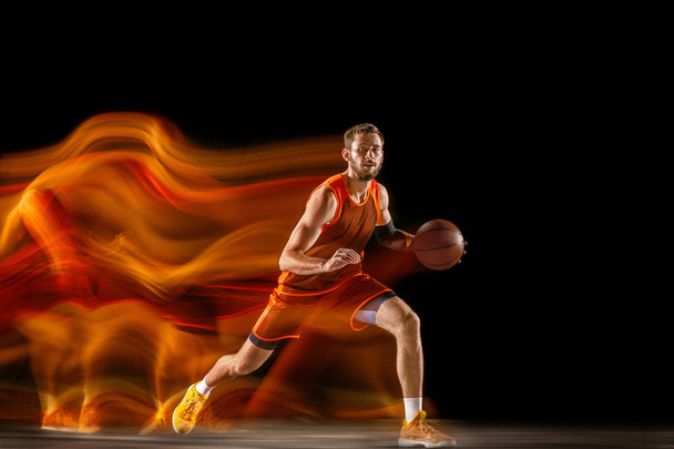 Young caucasian basketball player against dark background in mixed light - Fotó, kép