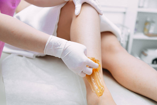 Young woman depilating legs with liquid sugar in spa center - Foto, Imagem