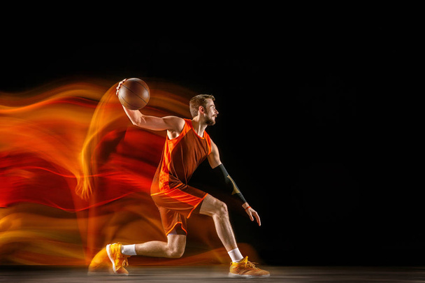 Young caucasian basketball player against dark background in mixed light - Фото, изображение