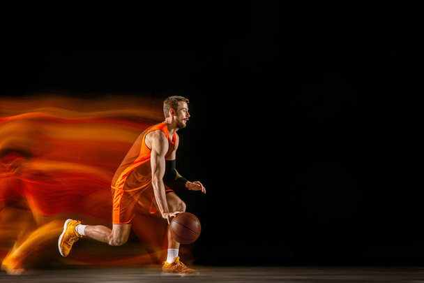 Young caucasian basketball player against dark background in mixed light - Foto, Imagen