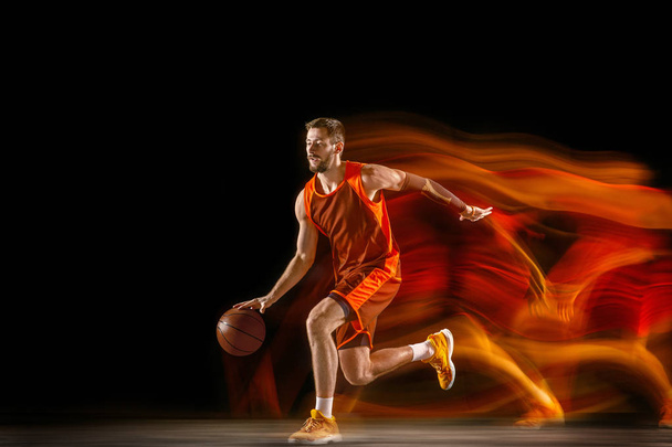 Young caucasian basketball player against dark background in mixed light - Фото, зображення