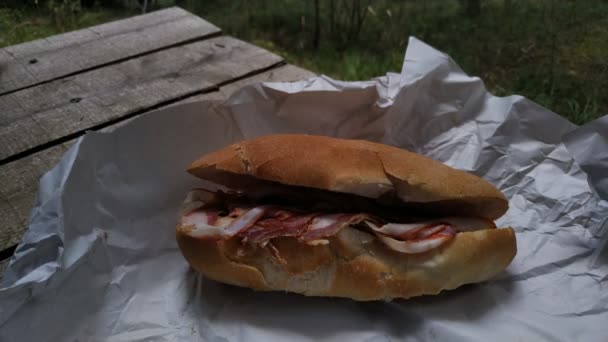 Een heerlijke salame witte stokbrood sandwich op houten tafel. Vlees vulling in wit brood verpakt in papier. - Video