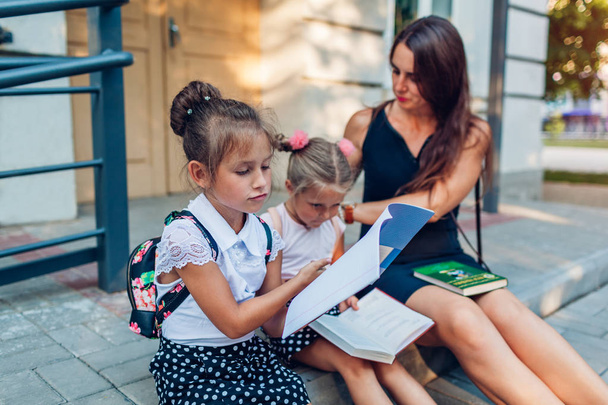 幸せな母親は授業の後に子供の娘たちに会った。小学校の屋外で本を読む子供たち. - 写真・画像
