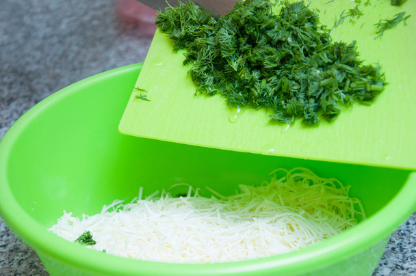 Grated cheese in a green bowl, with chopped dill on a green board.  Cooking food close up. - Foto, Imagen