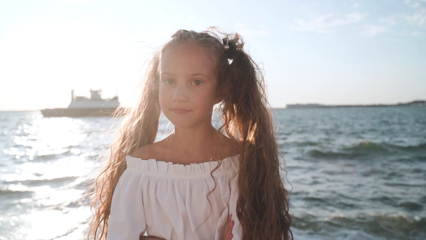 Μικρό κορίτσι στέκεται κοντά στη θάλασσα, σταυρωτά χέρια στο στήθος - Πλάνα, βίντεο