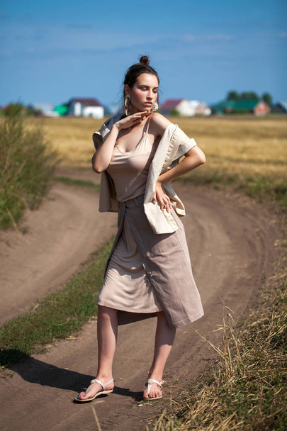 Beautiful girl in a beige suit posing on a background of haystac - Фото, изображение