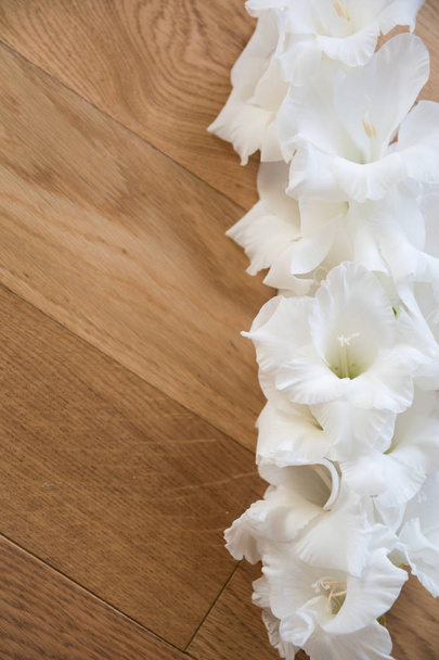 Valkoinen gladioli makaa kuvioitu puupinta. Puolella on tilaa kuvateksteille. Tervehdyskortti häät tai loma tervehdys. Yläkuva
 - Valokuva, kuva