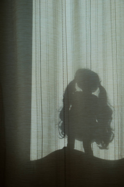 Colagem sobre o tema da sombra. Silhueta de uma menina através das cortinas. Uma boneca com o cabelo em pé num peitoril da janela. Abstração em tons castanhos
. - Foto, Imagem