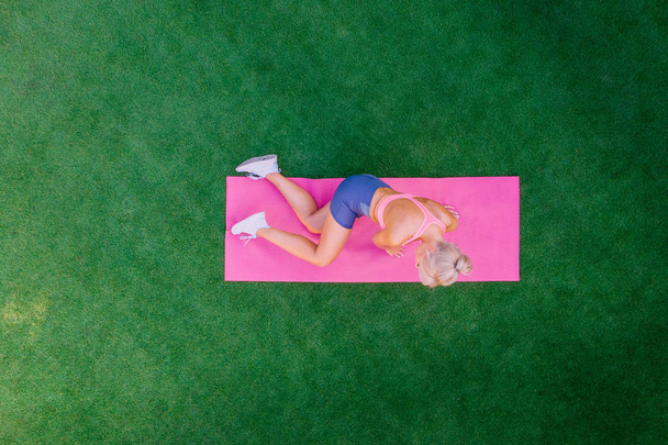 Top view woman doing fitness while lying on green grass on summer day, drone shot - Foto, afbeelding