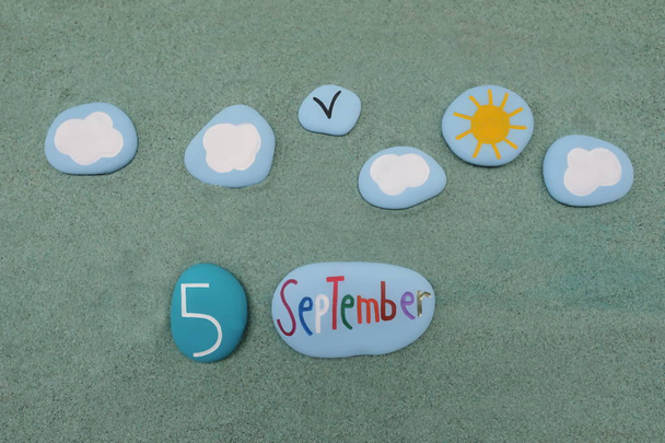 5 de septiembre, fecha del calendario compuesta con letras y números de piedra de color rojo sobre arena verde - Foto, imagen