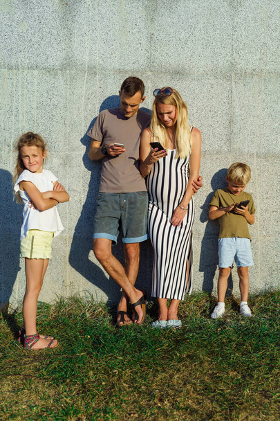 Foto de mujer, hombre e hijo con teléfonos en sus manos e hijas al lado de la pared de hormigón exterior
 - Foto, imagen