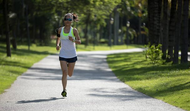 Deportiva mujer de fitness corriendo y escuchando música en el soleado parque
 - Foto, imagen