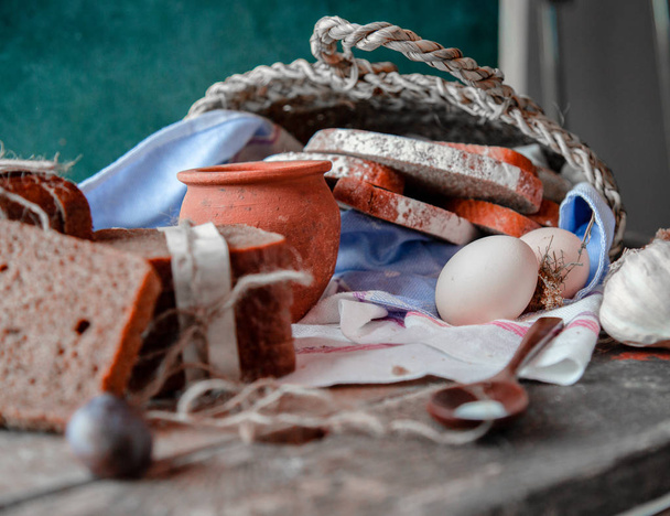 Koszyk z opakowanym plasterkami chleba wewnątrz, mleko i śliwki na zewnątrz na białym ręczniku, jajka i garlics wokół.  - Zdjęcie, obraz