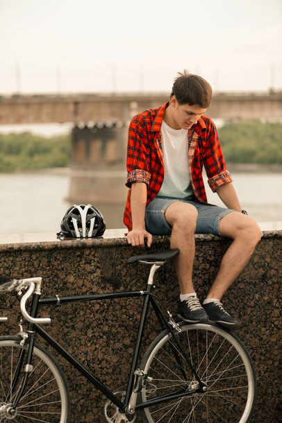 Young man in red shirt sitting on the stairs with a vintage bicycle near him - Foto, imagen