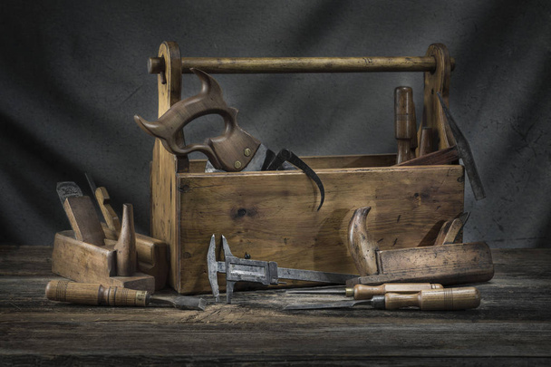 Asetelma - Vanha puinen vintage-työkalupakki, jossa vasarat, saha, taltat, lentokone ja pihdit kirvesmiehinä
 - Valokuva, kuva