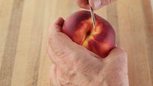 A man removes the peel from a peach over a cutting board. - Felvétel, videó