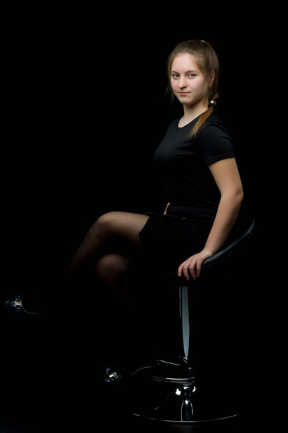Charming girl teenager sitting on a chair in the studio on a bla - Fotó, kép