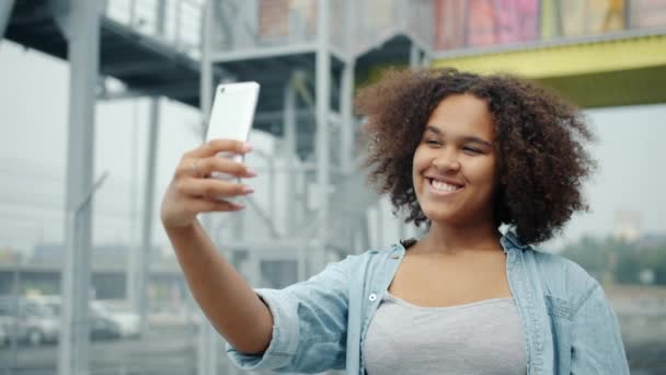 Slow motion of pretty African American woman taking selfie with smartphone outdoors - Кадри, відео