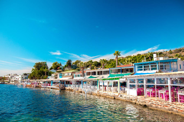 Vista de restaurantes de pescado o cafeterías y flores en la playa en Gumusluk, Bodrum ciudad de Turquía. Mar Egeo estilo sillas coloridas, mesas y flores en la ciudad de Bodrum Marina cerca del hermoso mar Egeo
. - Foto, imagen