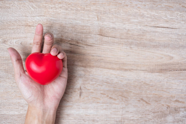άνθρωπος κρατώντας κόκκινο σχήμα καρδιάς σε ξύλινο φόντο. Υγειονομική περίθαλψη, Li - Φωτογραφία, εικόνα