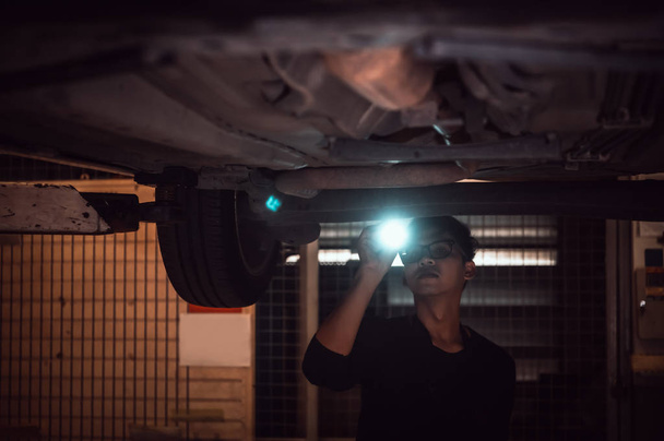 シャシの下で車を調べるために懐中電灯を輝く孤独なアジアの男性 - 写真・画像