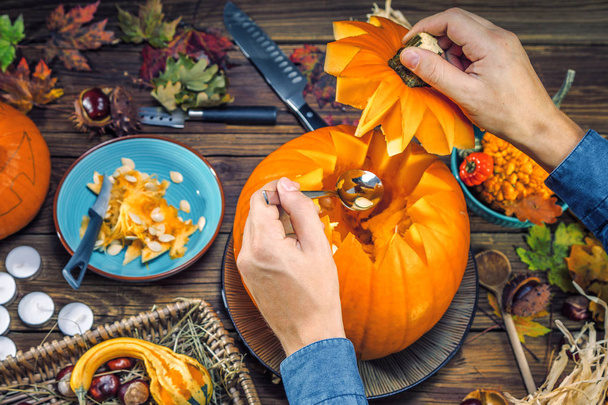 partial view of person carving halloween pumpkin heads, pumpkins on wooden background  - 写真・画像