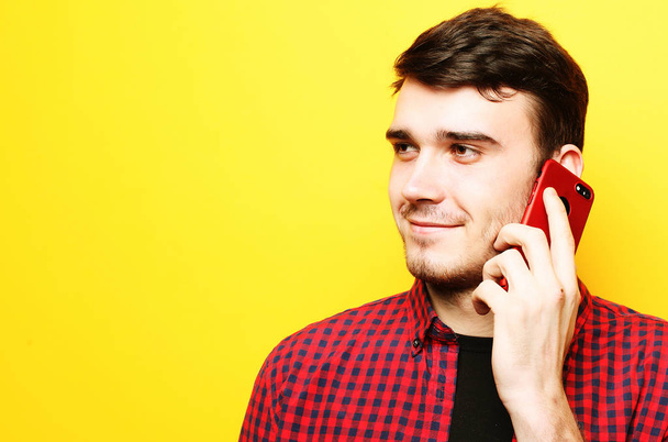 Happy young man talking on cell phone over yellow background - Foto, Imagen