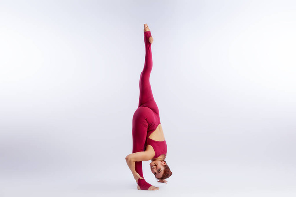 Beautiful slim woman in sports overalls  doing yoga, standing in an asana balancing pose   on white  isolated background. The concept of sports and meditation. - Photo, Image