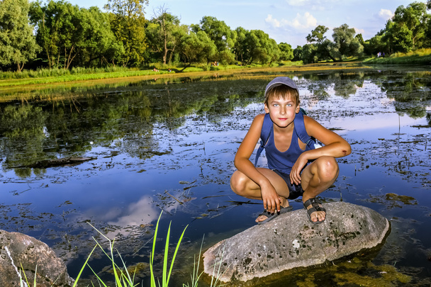 The boy is sitting on a rock by the Lake - Foto, Bild
