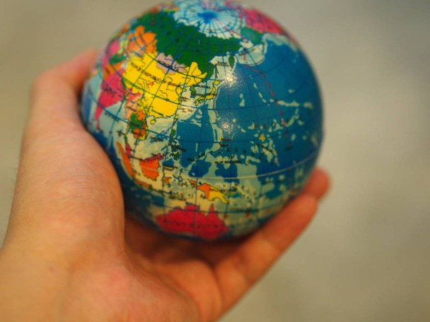Close Up Hand holding a Mini Globe with Wooden Table Background. - Фото, изображение