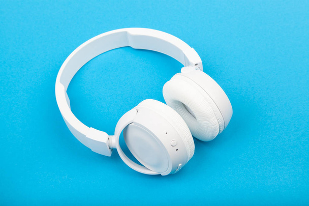 Vezeték nélküli fehér fejhallgató kék háttérrel. Zenei koncepció. Fülhallgató kék háttérrel.  - Fotó, kép