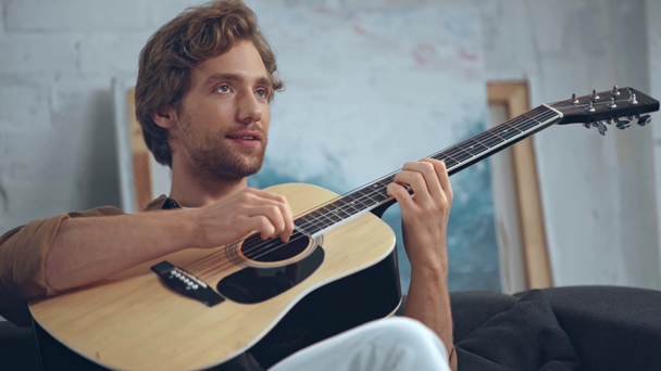 young man playing acoustic guitar on sofa - Кадри, відео