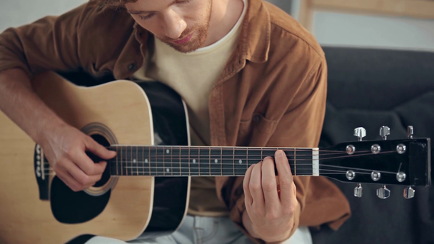 κιθαρίστας παίζει ακουστική κιθάρα στον καναπέ - Πλάνα, βίντεο