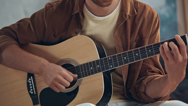 wykadrowany widok człowieka grających na gitarze akustycznej na kanapie - Materiał filmowy, wideo