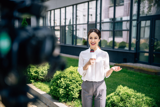selective focus of attractive journalist holding microphone and speaking outside  - Photo, image