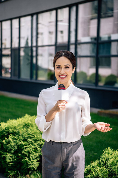 journaliste attrayant en tenue formelle tenant microphone et parlant à l'extérieur
  - Photo, image