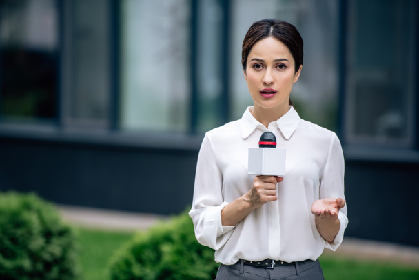 attractive journalist in formal wear holding microphone and speaking outside  - Foto, Imagen