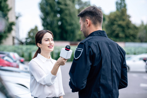 journalist holding microphone and talking with handsome policeman in uniform - Fotoğraf, Görsel