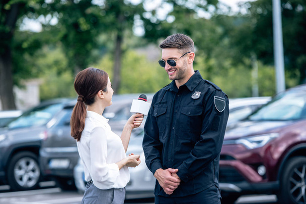 periodista sosteniendo micrófono y hablando con guapo policía en uniforme
 - Foto, imagen