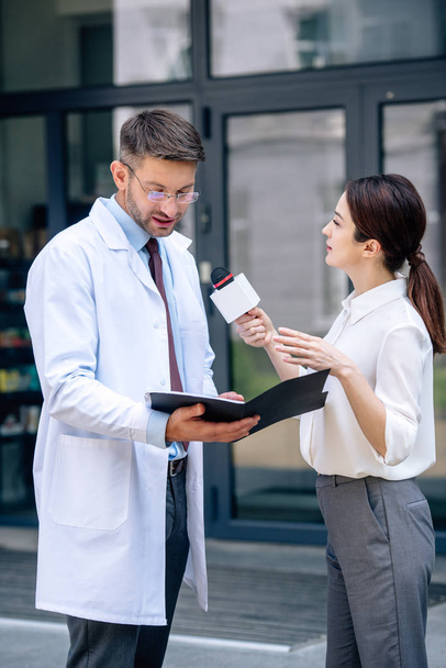 journalist holding microphone and talking with handsome doctor in white coat - Foto, Bild