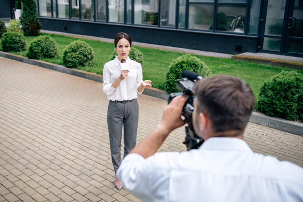 selektivní zaměření atraktivního novináře, který drží mikrofon a kameraman a natáčet ji venku  - Fotografie, Obrázek