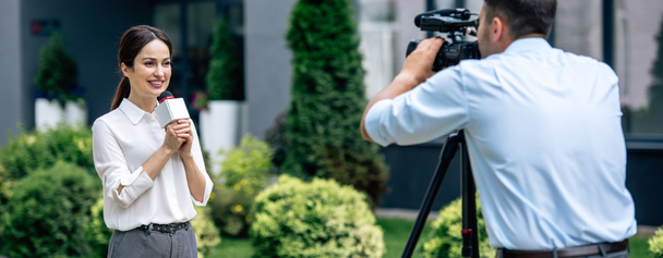 scatto panoramico di attraente giornalista con microfono in mano e cameraman che la fotografa fuori
  - Foto, immagini