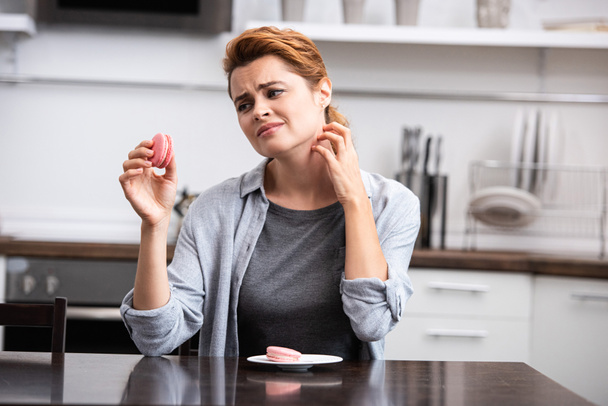 woman looking at pink dessert while scratching neck  - Photo, Image