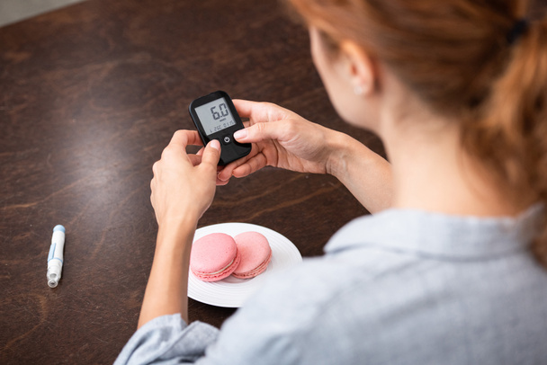 selective focus of woman holding glucose monitor near sweet dessert  - Photo, Image