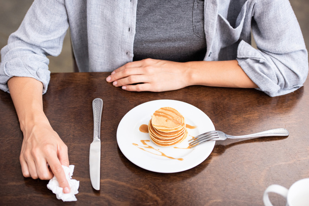 overhead view of woman sitting near table with sweet pancakes on plate   - Foto, afbeelding