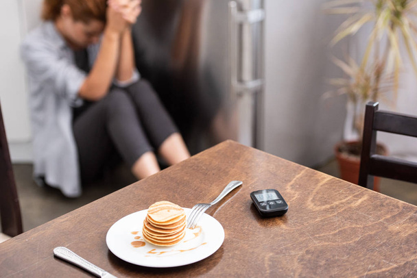 selektiver Fokus von leckeren Pfannkuchen auf dem Tisch in der Nähe von Glukosemesser und Frau auf dem Fußboden  - Foto, Bild