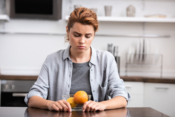 upset woman looking at glass bowl with fruits  - Photo, Image