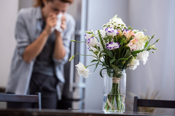 foco seletivo de flores em vaso perto de mulher espirrando no tecido
  - Foto, Imagem