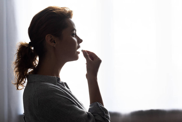 side view of attractive woman taking pill at home  - Photo, Image