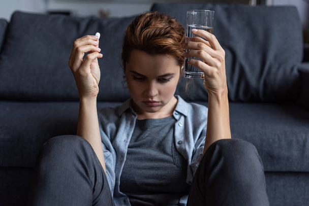 rozčilená a nemocná žena držící pilulku a sklenici vody  - Fotografie, Obrázek